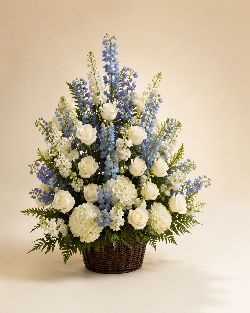 Blue Ridge sympathy basket with white roses, blue delphinium, white hydrangeias, and white stock in a dark wicker basket