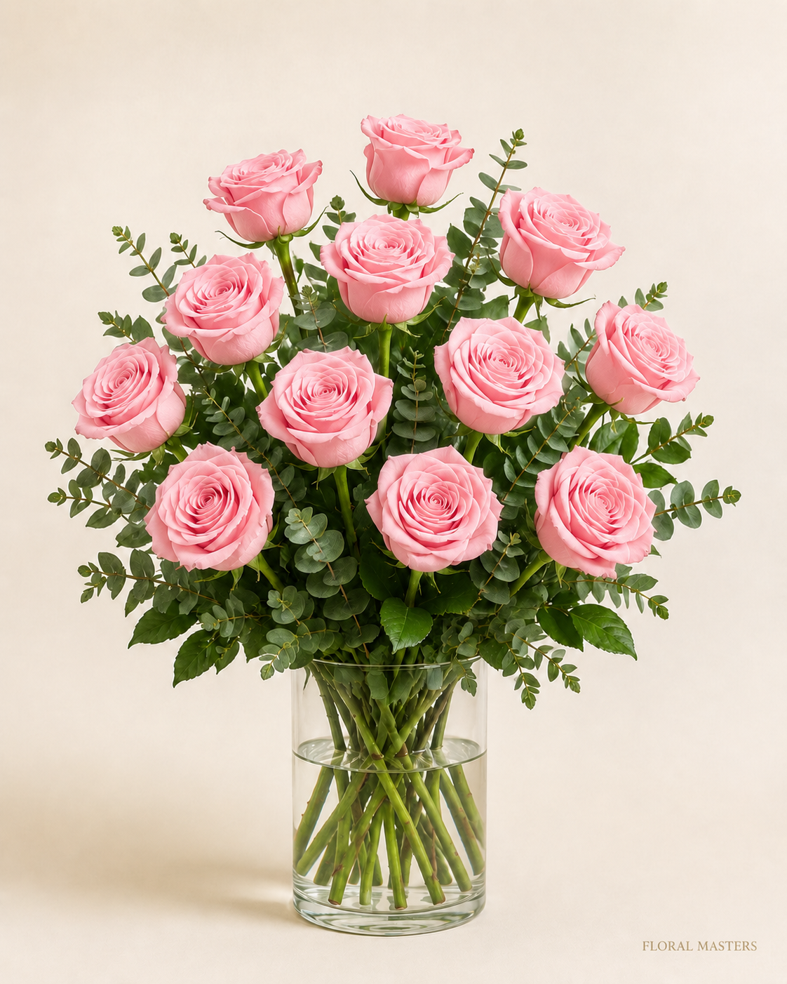 12 soft pink roses with greenery in a clear glass vase