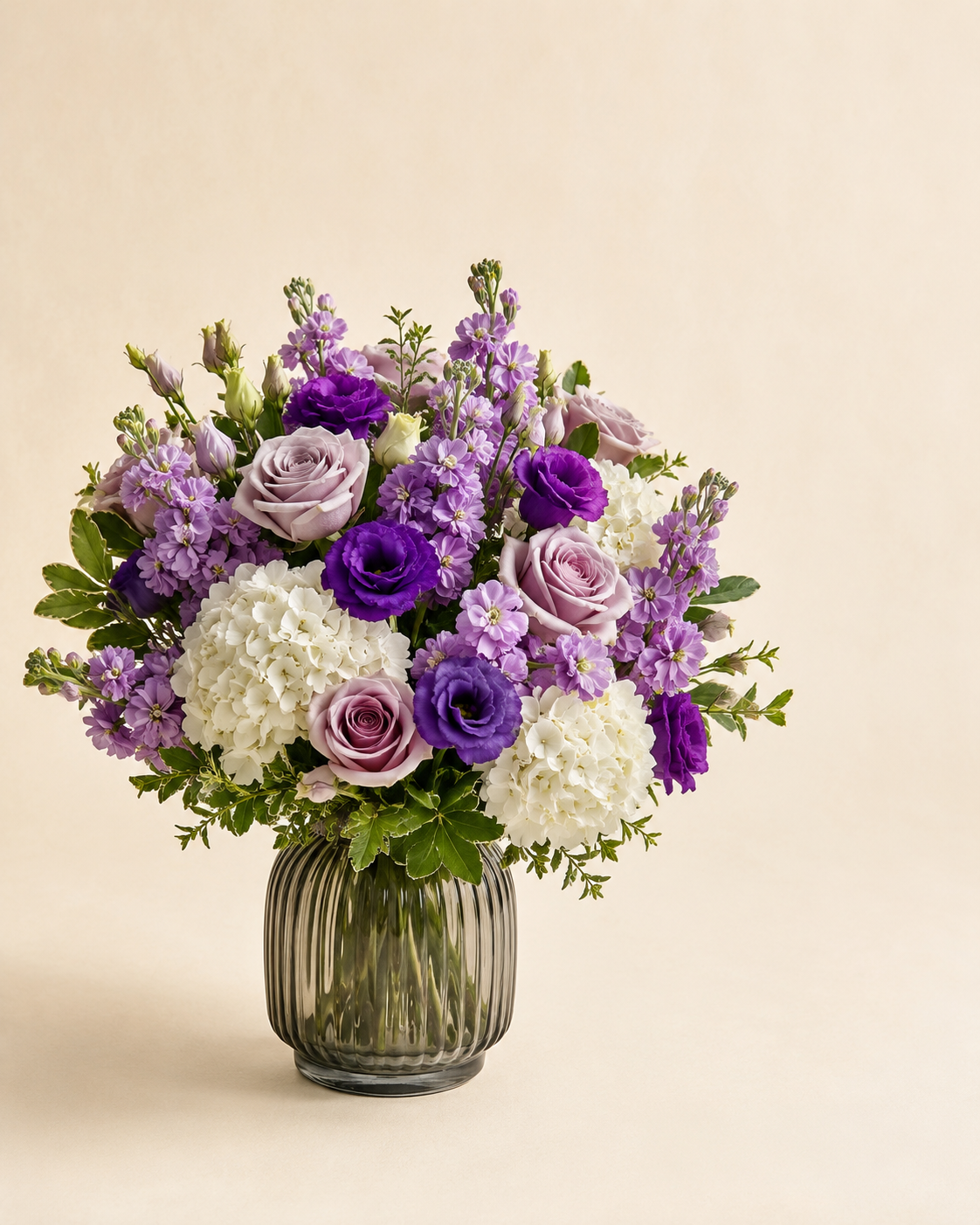 Lavender Window sympathy arrangement with lavender roses, lavender stock, purple lisianthus, and white hydrangeias in a smoke-glass vase
