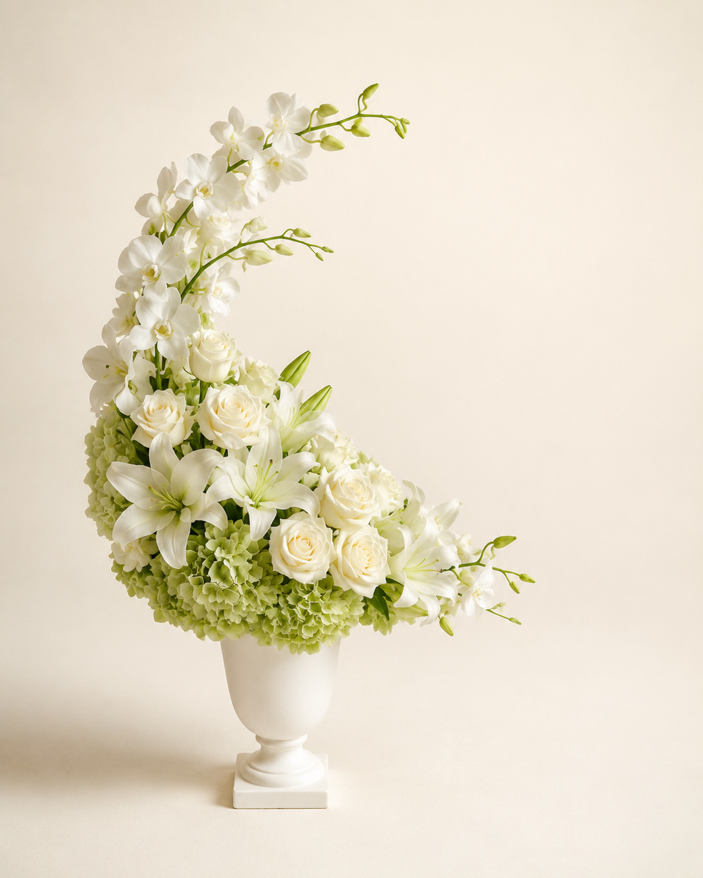 Moonlit Orchid Tribute with white dendrobium orchids, white roses, white lilies, and green hydrangeas in a matte-white urn vase