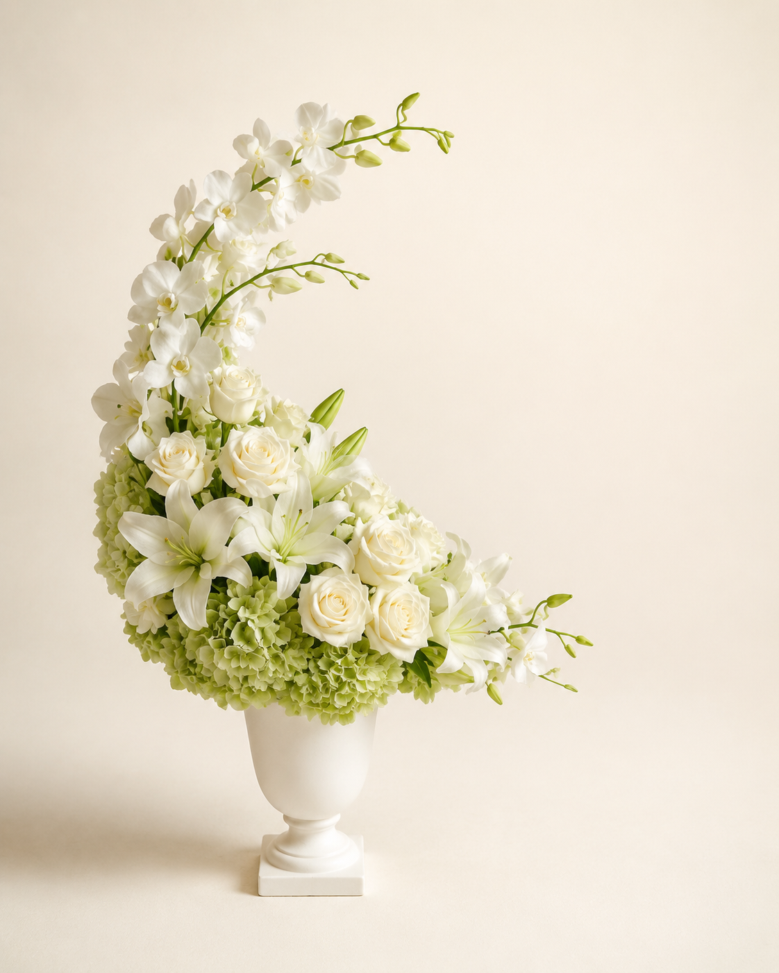 Moonlit Orchid Tribute with white dendrobium orchids, white roses, white lilies, and green hydrangeas in a matte-white urn vase