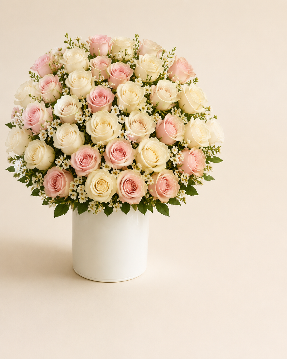 Pearl Blush Thirty-Six with ivory and blush roses and white waxflower in a pearl-white ceramic cylinder