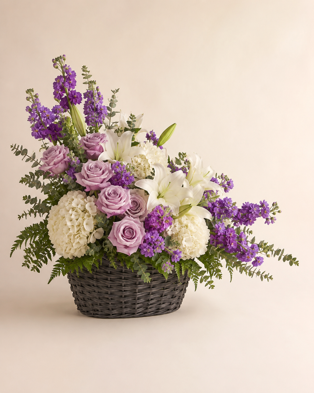 Plum and Pearl sympathy basket with lavender roses, purple stock, white hydrangeas, and white lilies in a charcoal wicker basket