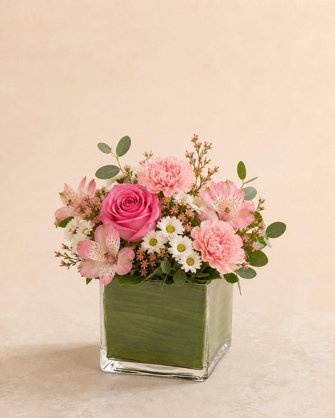 Rosewater Charm - Standard compact pink carnations, alstroemeria, cream mini mums and pink roses in a leaf-lined glass cube