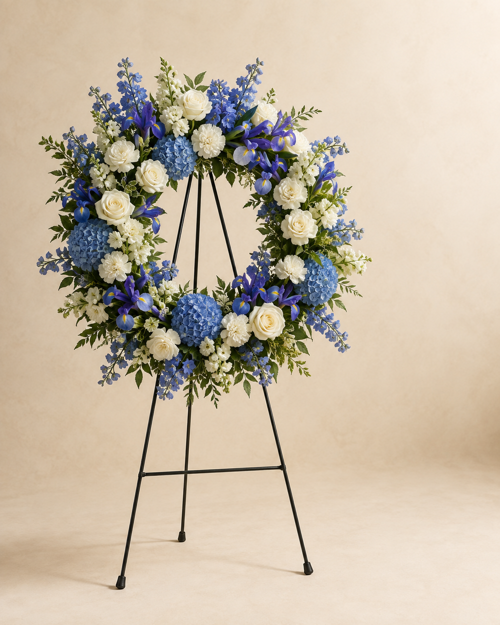 Sapphire Haven sympathy wreath with white roses, carnations, stock, blue hydrangea, delphinium, and iris on an easel