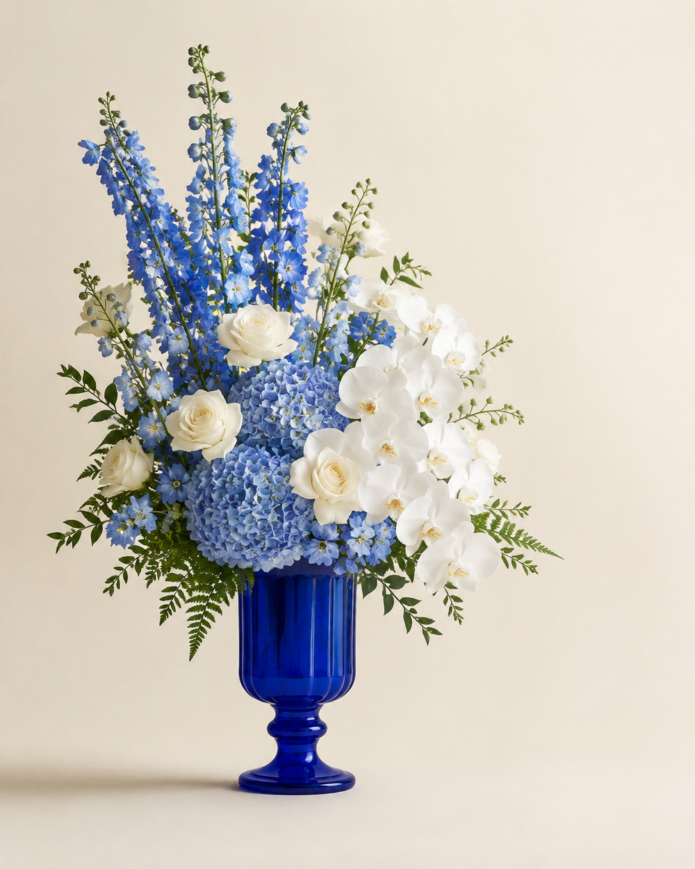 Sapphire Orchid Gallery with blue hydrangeas, blue delphinium, white orchids, and white roses in a cobalt glass pedestal vase