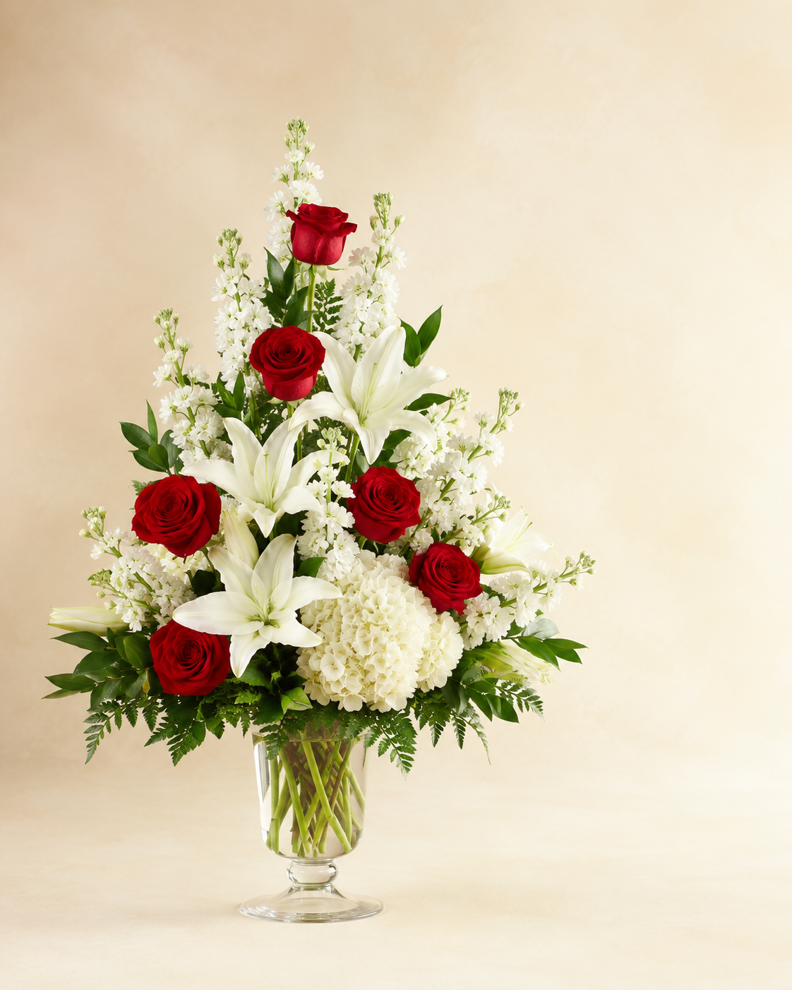 Scarlet and Snow sympathy tribute with red roses, white Oriental lilies, white hydrangeas, and white stock in a clear pedestal vase