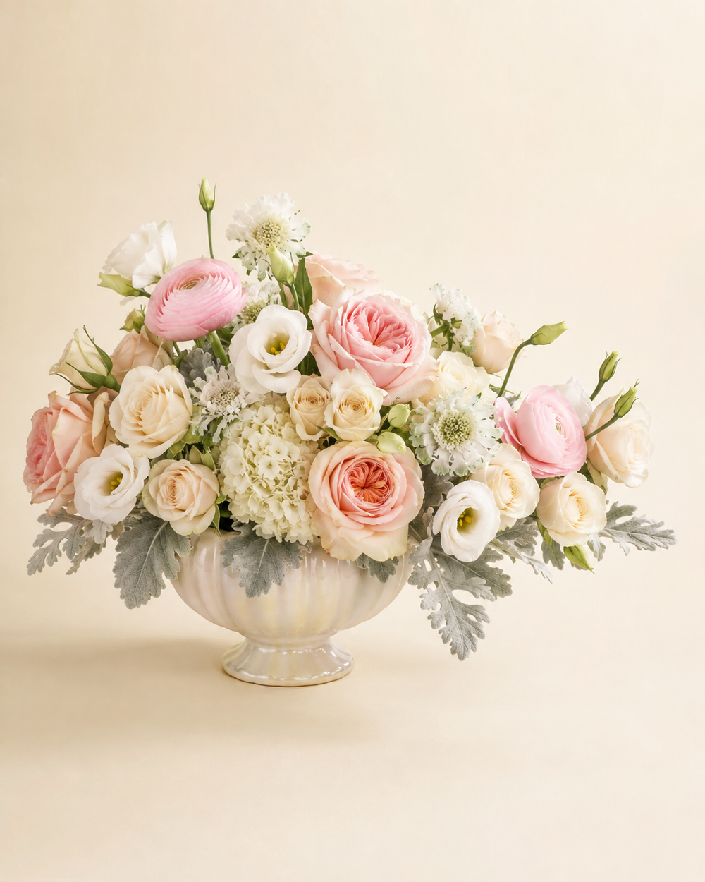 Softest Goodbye Compote with blush garden roses, ivory spray roses, white lisianthus, pale-pink ranunculus, hydrangea, scabiosa, and dusty miller in a pearl ceramic compote