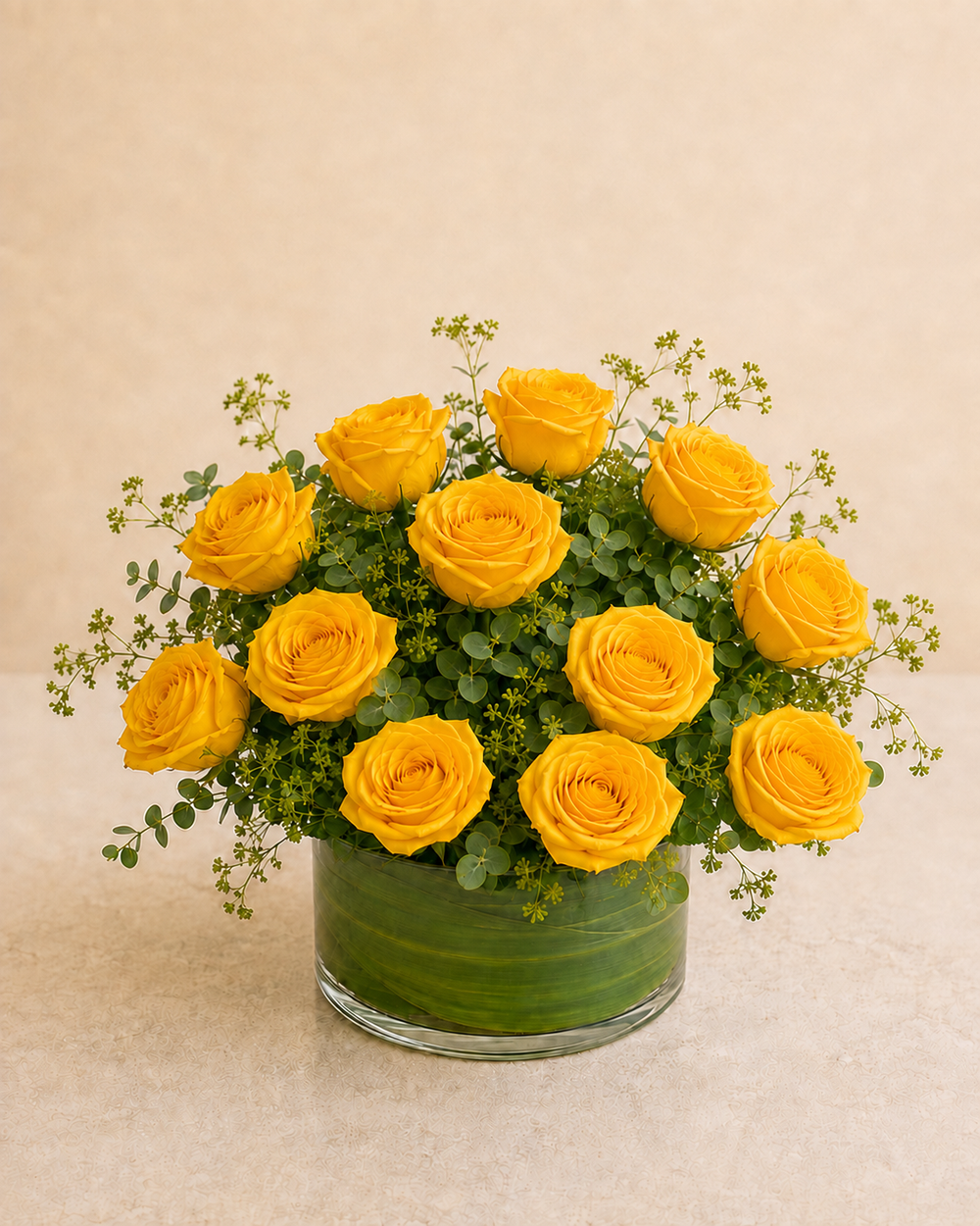 Exactly 12 yellow roses in a low leaf-wrapped clear glass vase
