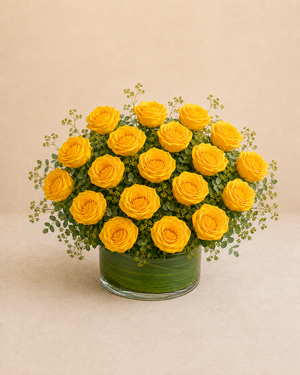 Exactly 18 yellow roses in a low leaf-wrapped clear glass vase