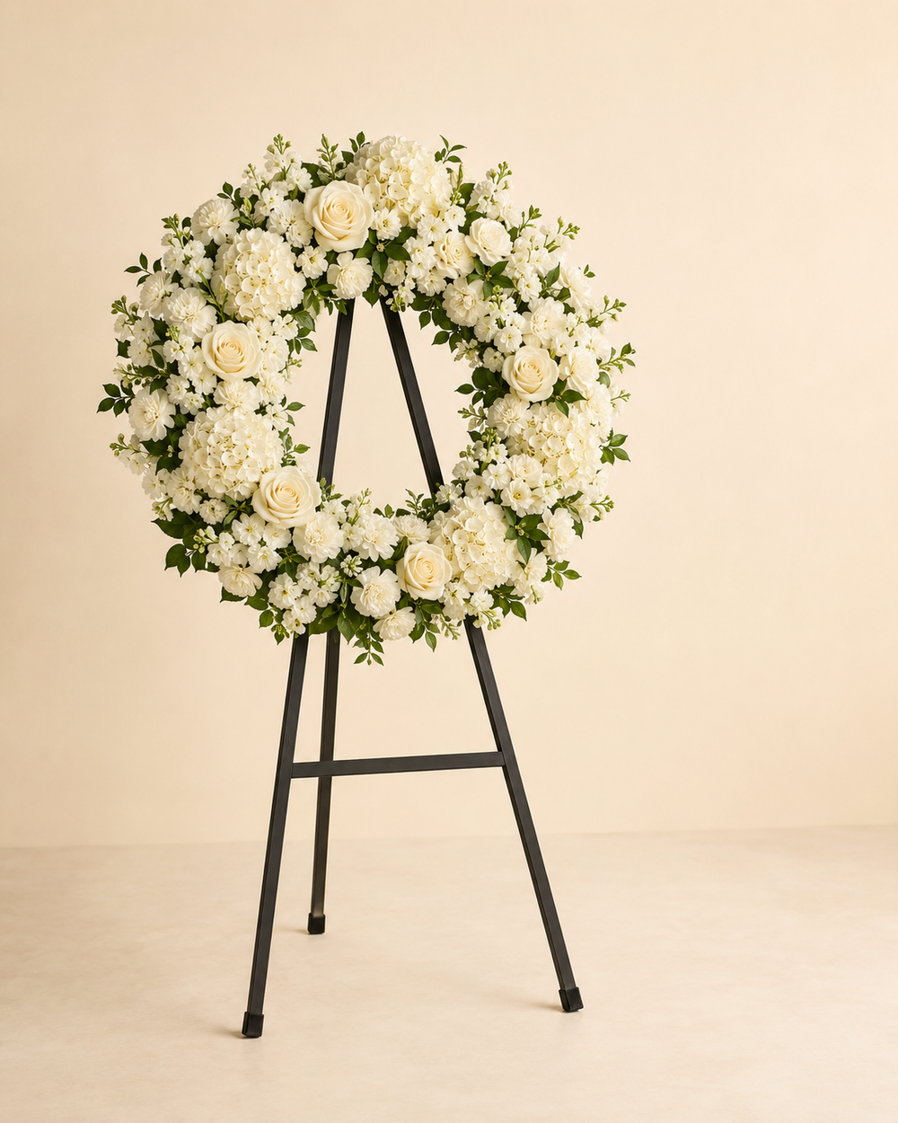 Unbroken Ivory open-center sympathy wreath with white roses, carnations, hydrangeas, and stock on an easel