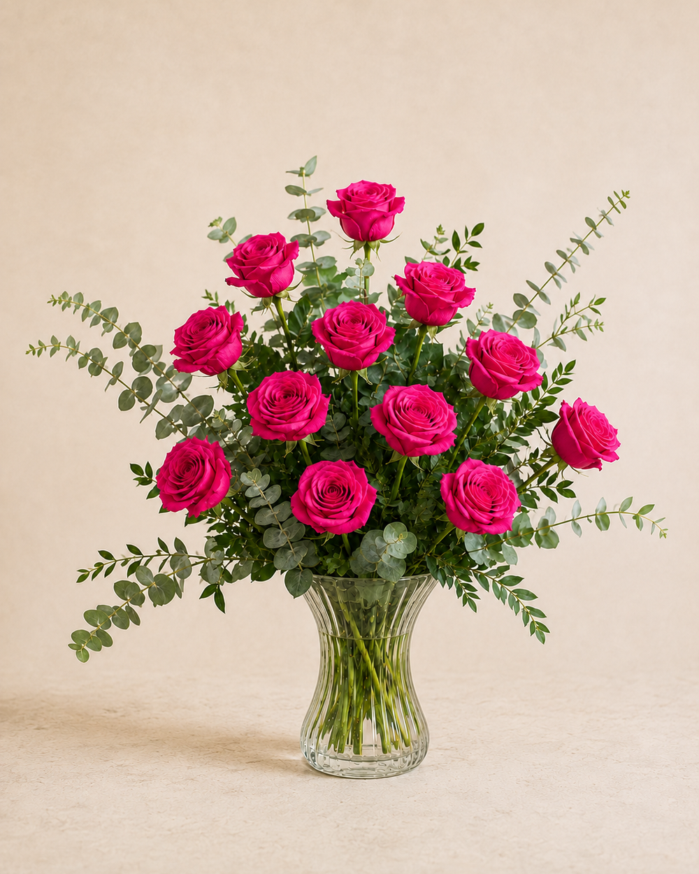 Exactly 12 hot pink roses in a clear fluted hourglass vase