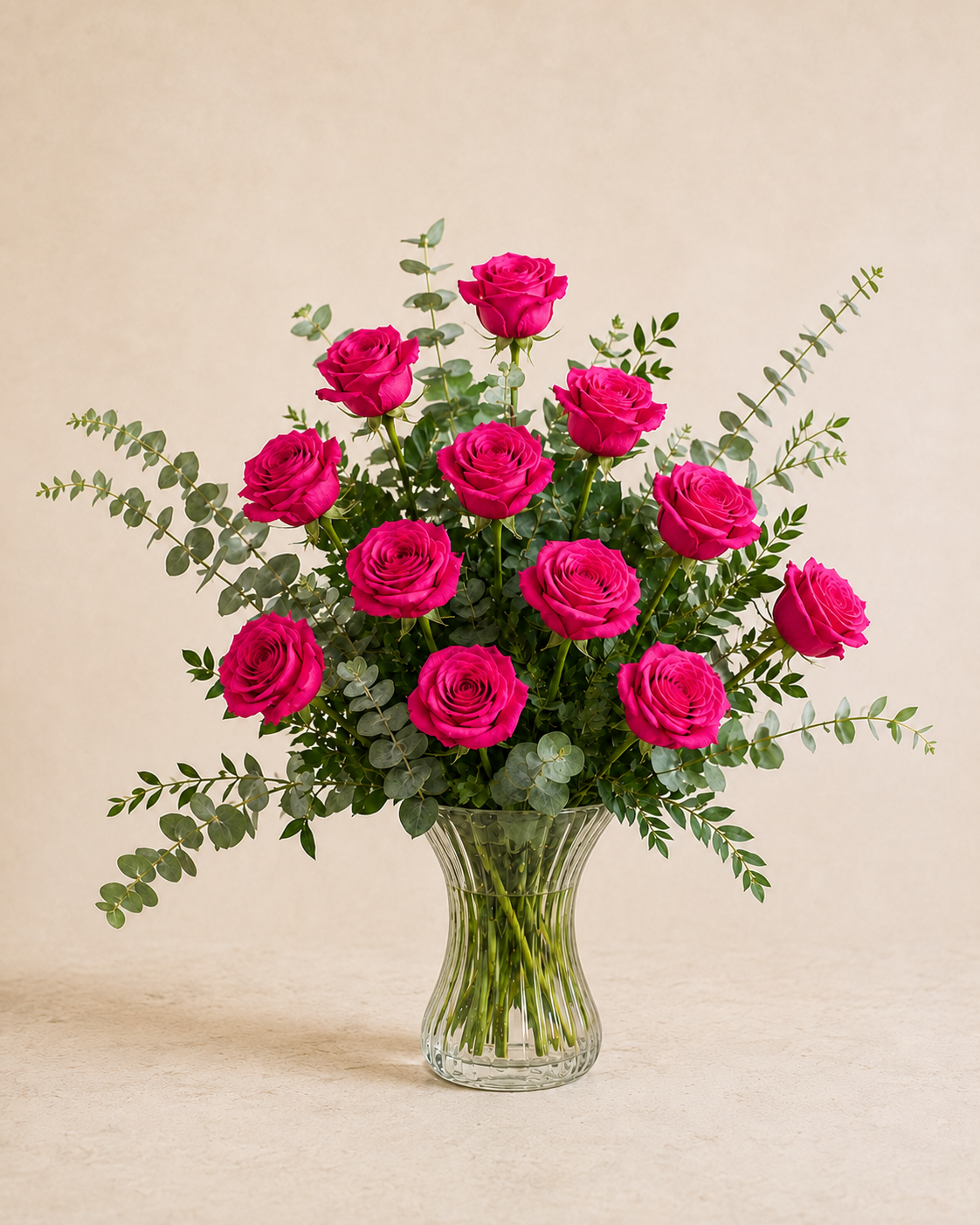 Exactly 12 hot pink roses in a clear fluted hourglass vase